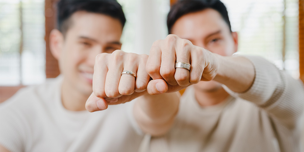 Two grooms showing off their wedding rings